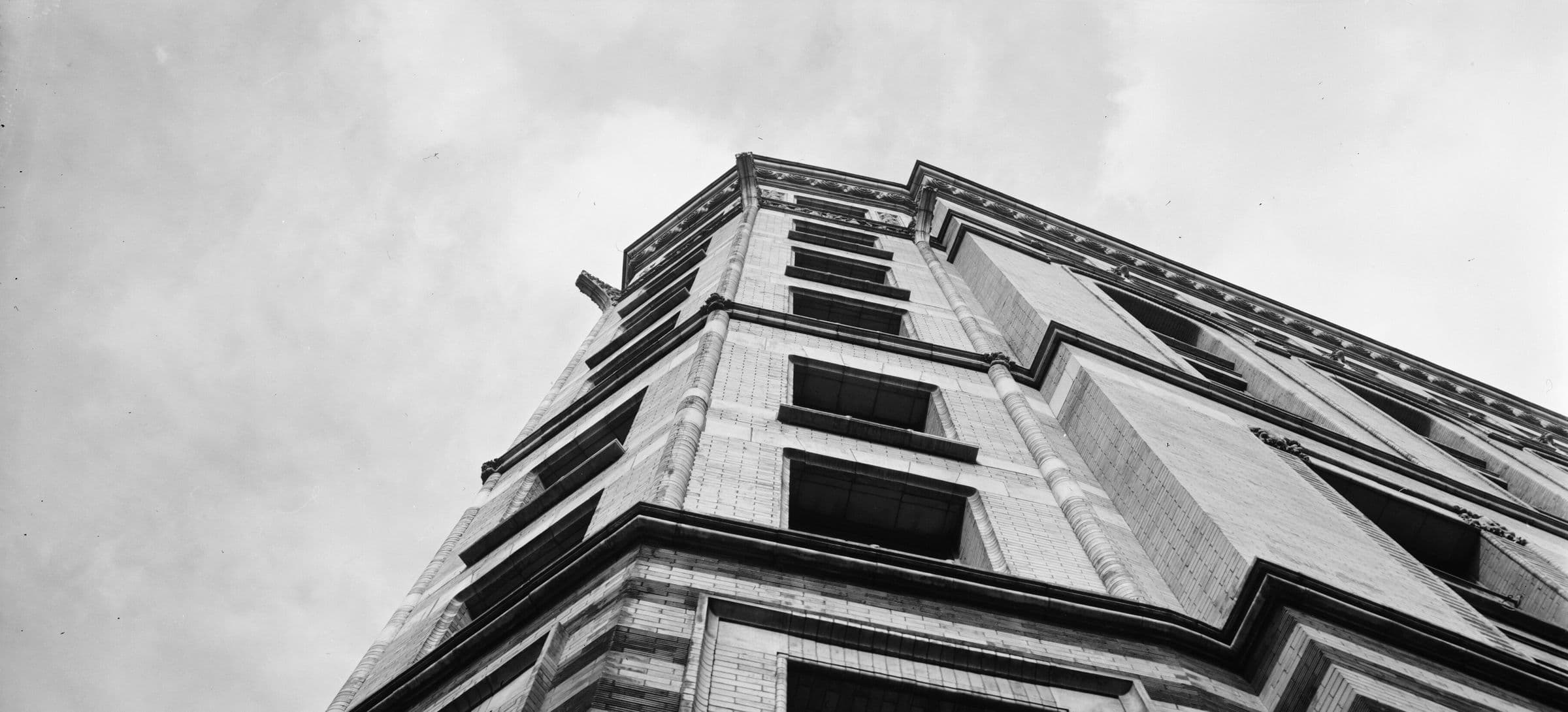 The upper corner of an early high-rise office building, photographed from street level against an open sky.